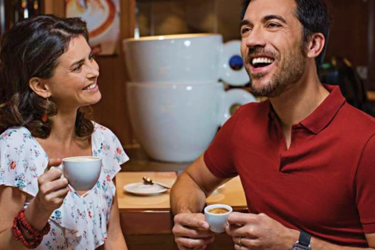 Couple smiling while enjoying coffee together in a modern café setting on a cruise ship