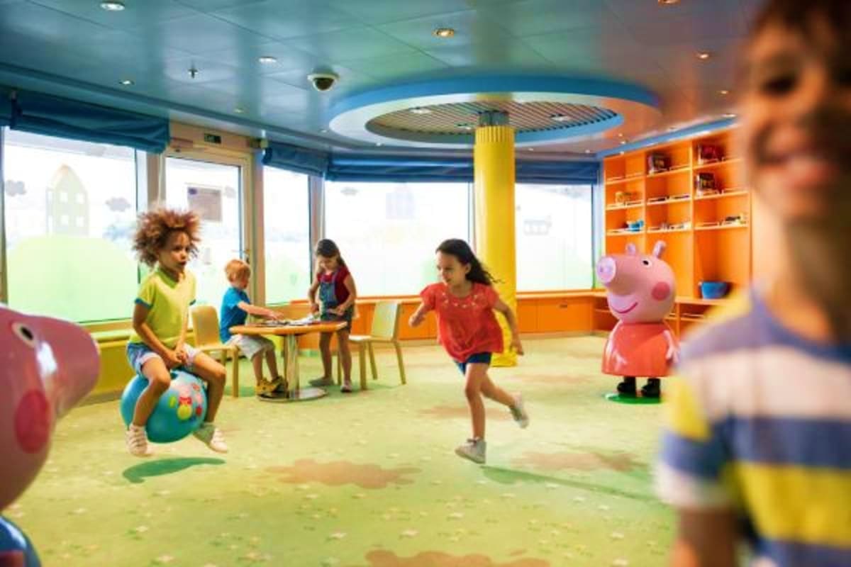 Children's play area on Costa Fascinosa with kids playing, colorful orange shelving, yellow support column, and large windows