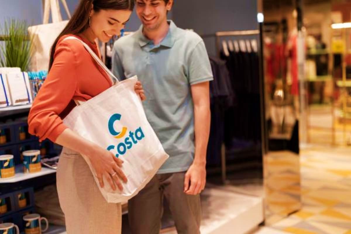 Couple examining Costa branded shopping bag in retail store with clothing displays and merchandise in background