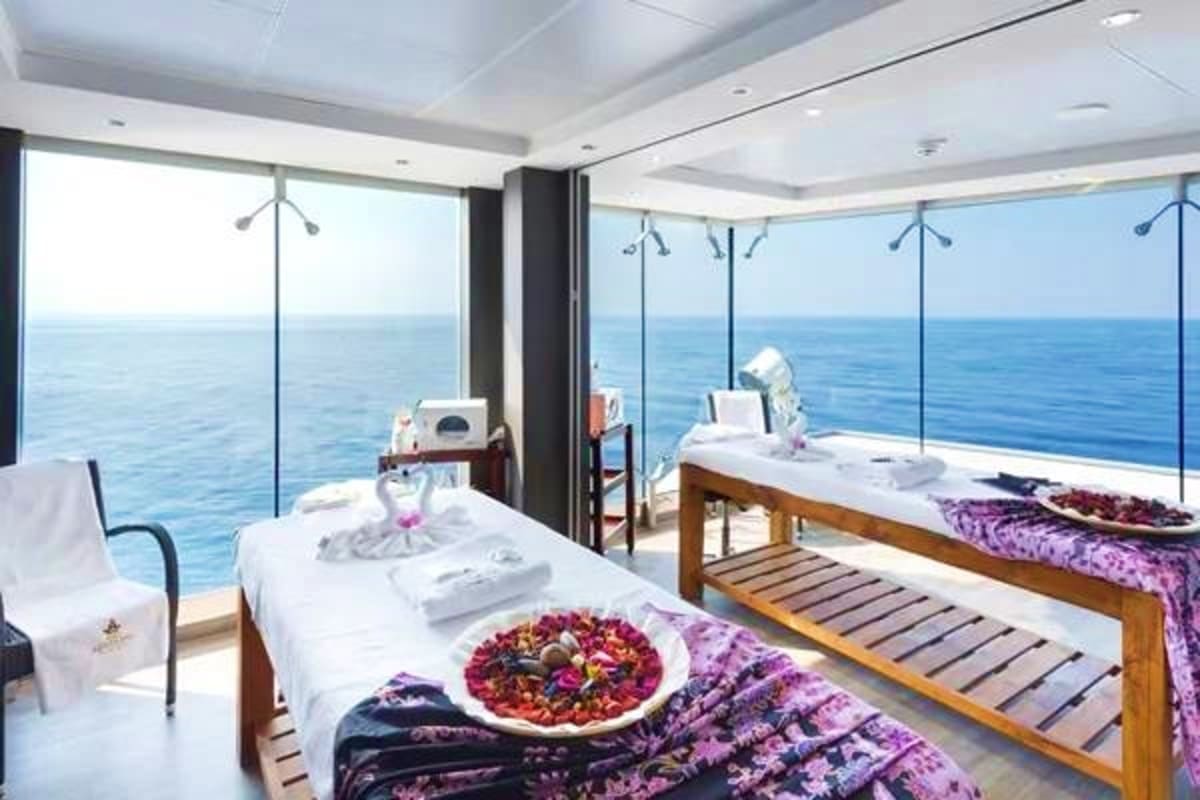Luxury cruise ship spa room with two massage tables, ocean view windows, and purple linens overlooking the sea