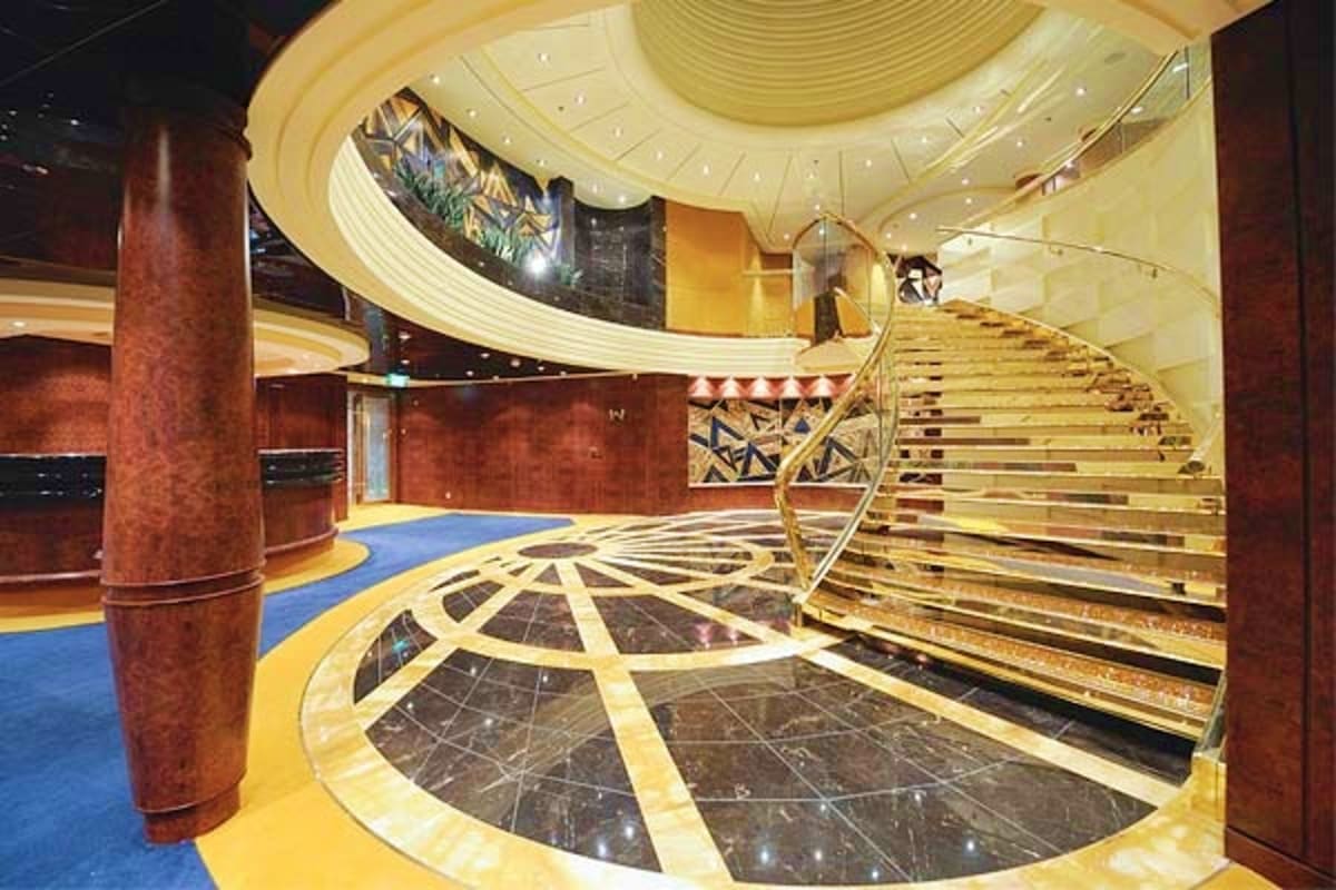 Luxurious cruise ship interior atrium with curved ceiling, grand staircase, marble flooring, and red columns