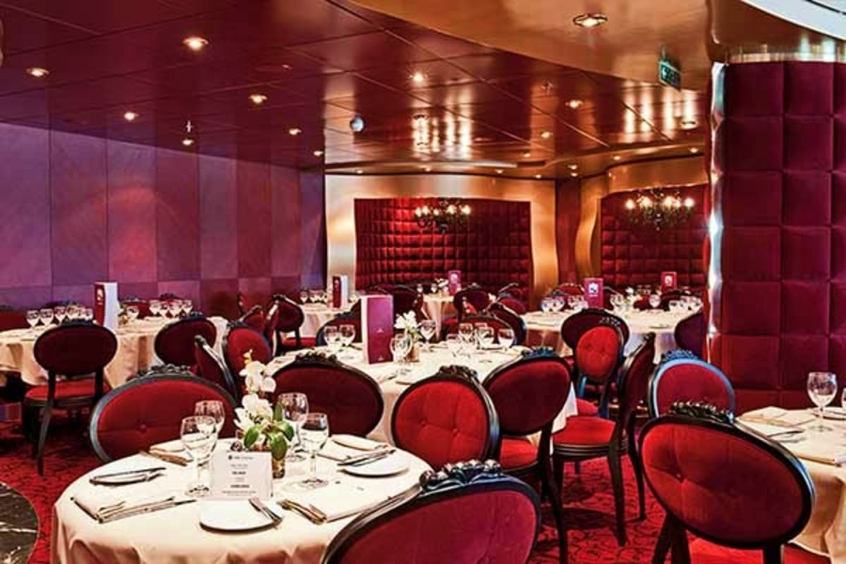 Elegant dining room on MSC Fantasia cruise ship with red velvet chairs, white tablecloths, and burgundy quilted wall panels l