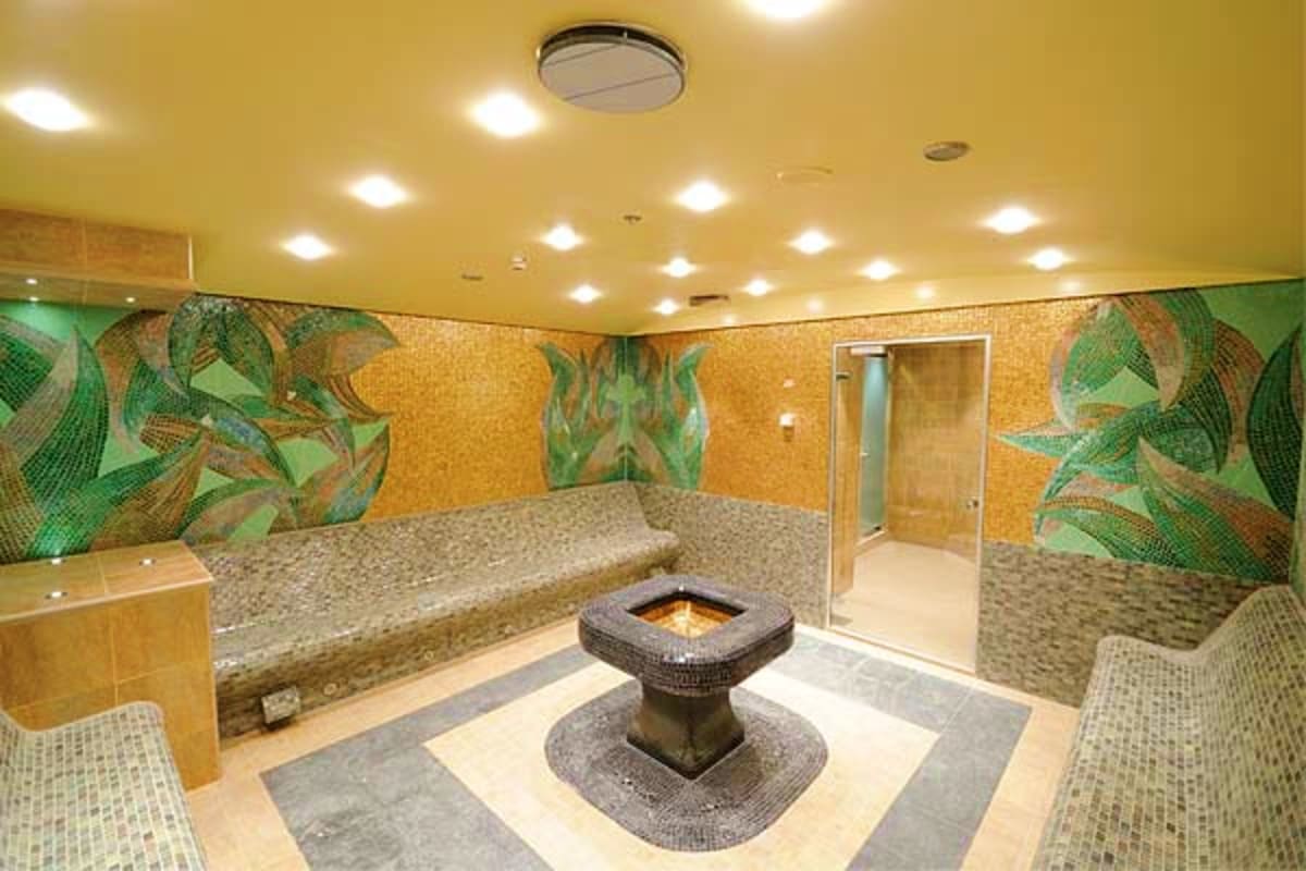 Luxury spa relaxation area with heated stone benches, central fire feature, decorative mosaic wall tiles, and ambient lightin