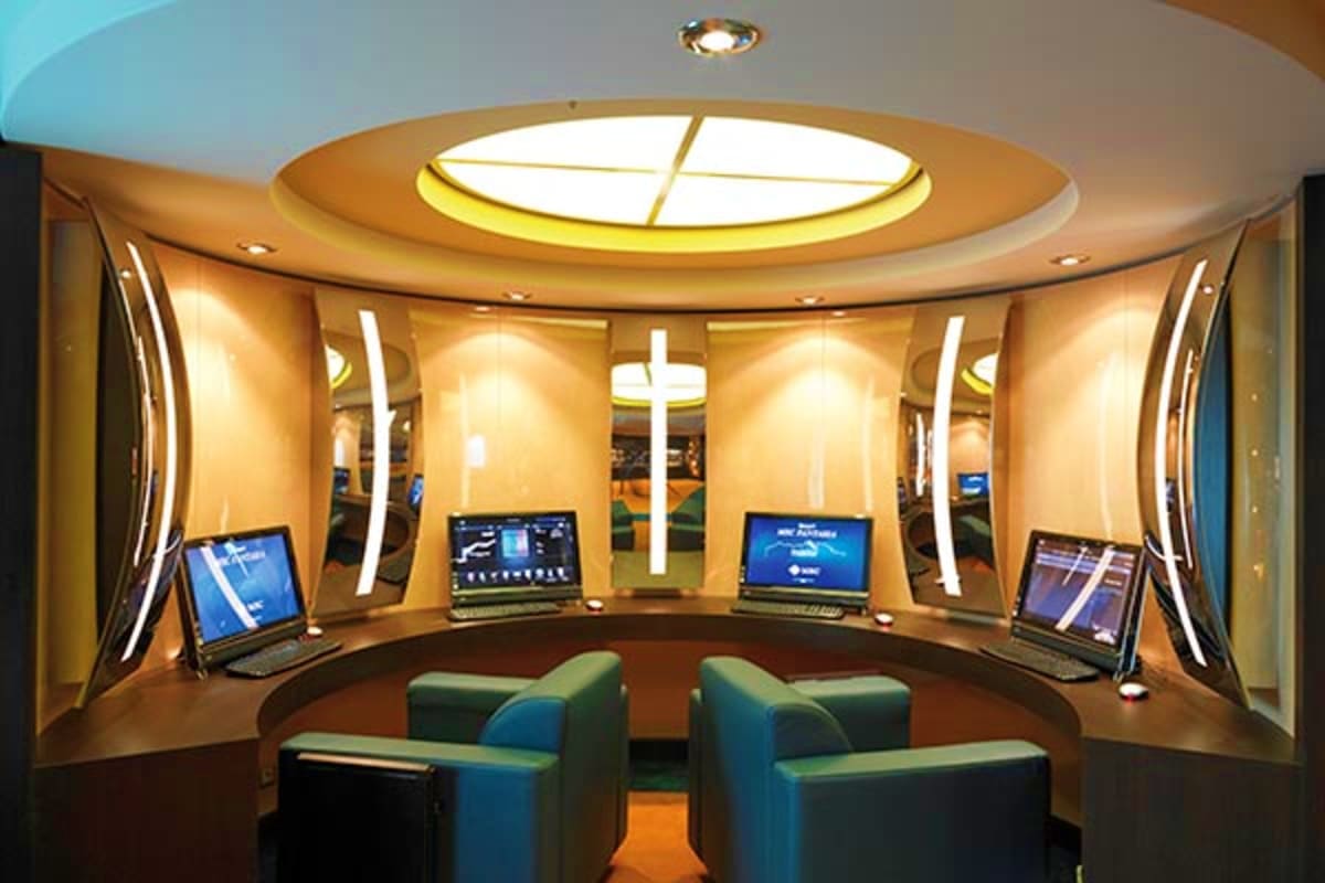 Modern cruise ship cabin command center with curved walls, blue chairs, multiple computer monitors, illuminated ceiling skyli