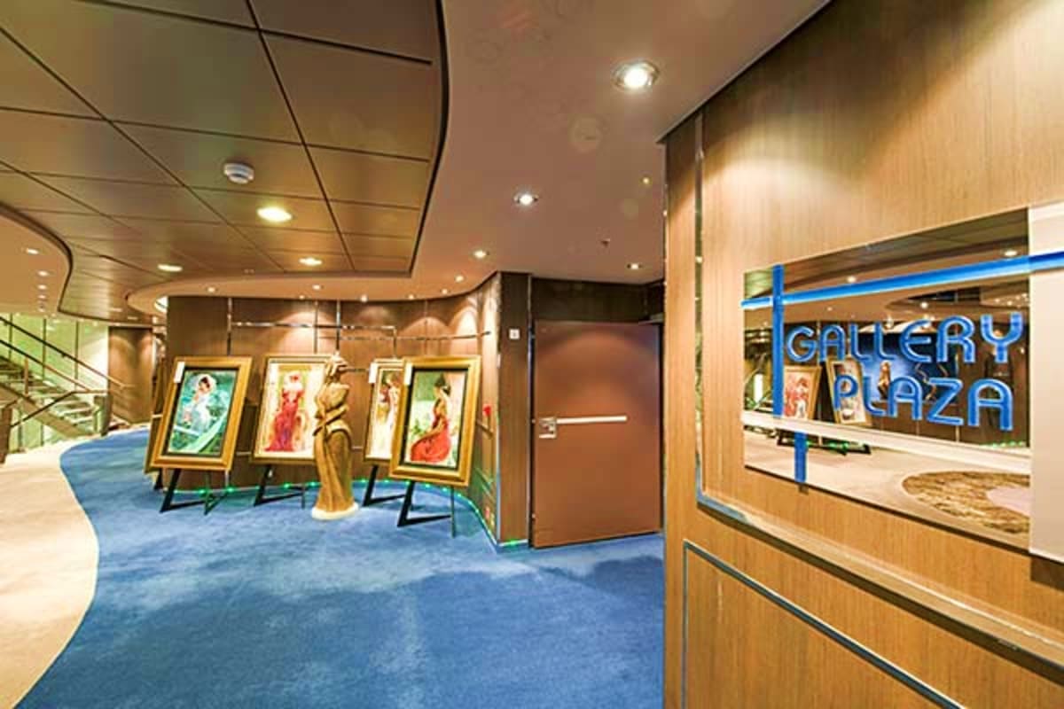 Modern cruise ship gallery lounge with framed artwork displays, wooden paneling, and blue carpeting featuring Gallery Plaza s