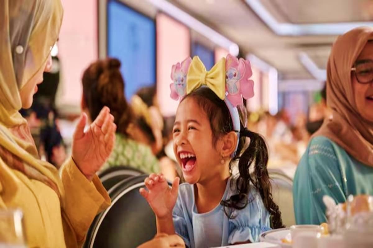 Three Nights Magical Disney Getaway Young child wearing yellow bow headband smiling at woman during Disney cruise ship dining experience with other passengers