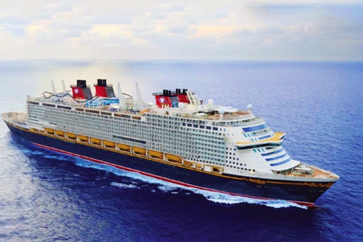 Four Nights Disney Adventure Magical Asian Escape Large white and black cruise ship with red funnels sailing on blue ocean water under cloudy sky