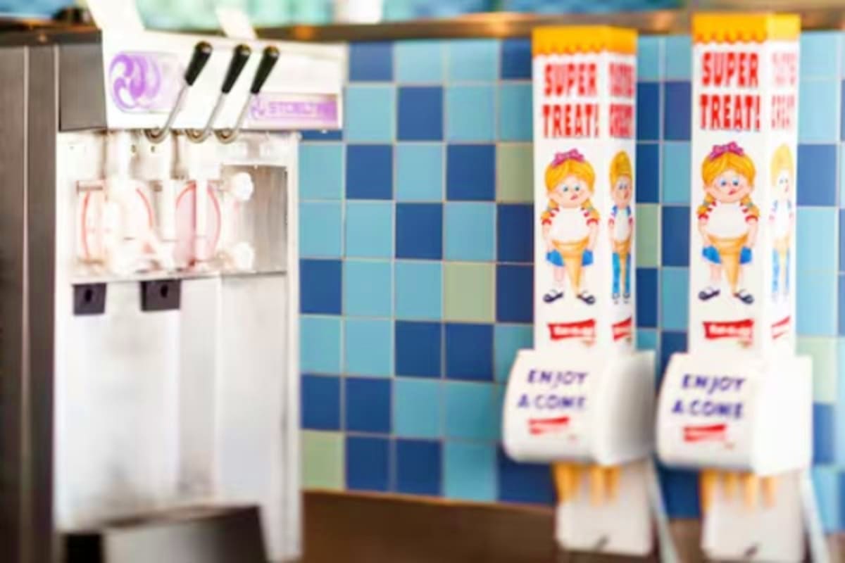 Vintage ice cream parlor with white soft-serve machine and cartoon character branded ice cream cup boxes against blue checker