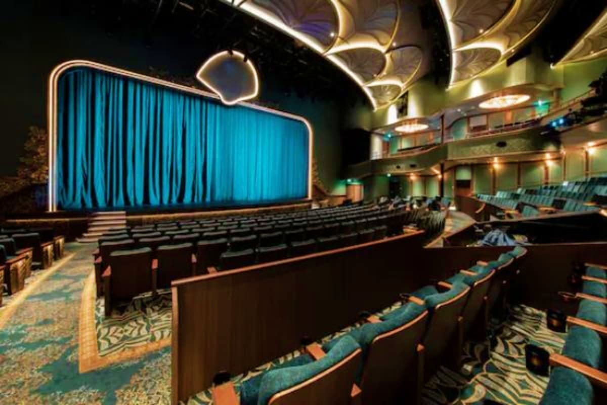 Modern movie theater interior with blue curtained screen, rows of teal seats, and decorative ceiling lighting