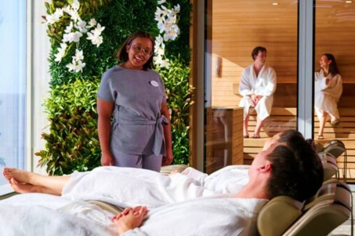 Spa therapist smiling at client relaxing on massage bed with green living wall and white flowers in luxury spa setting