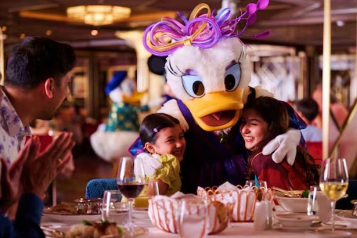 Daisy Duck character in purple bow greeting young children at dining table during Disney cruise ship dinner