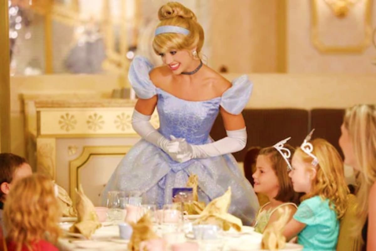 Character in blue ball gown greeting young children at elegant dining table in palace setting