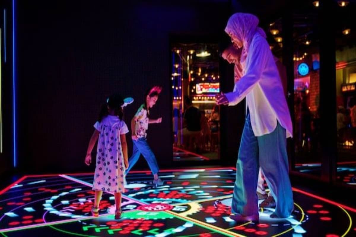 Adult and children playing on illuminated interactive floor in modern arcade entertainment venue at night