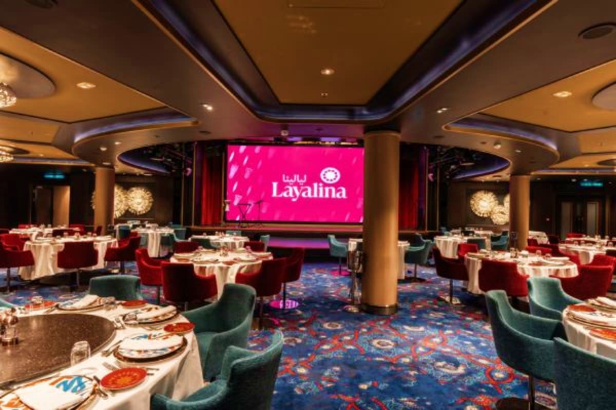 Layalina restaurant interior with round dining tables, red and teal chairs, white linens, and large pink illuminated Layalina