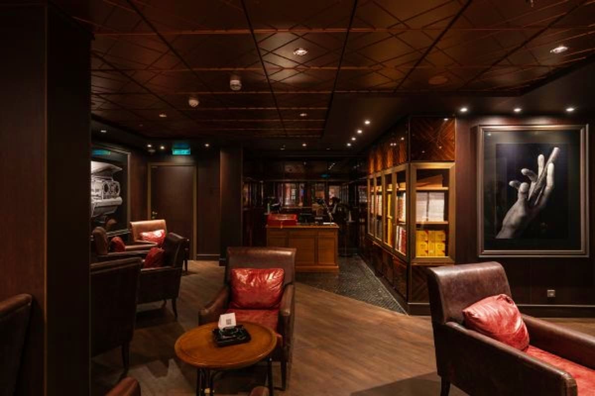 Luxurious dark-toned lounge interior with leather seating, wooden accents, ambient lighting, and framed artwork on walls