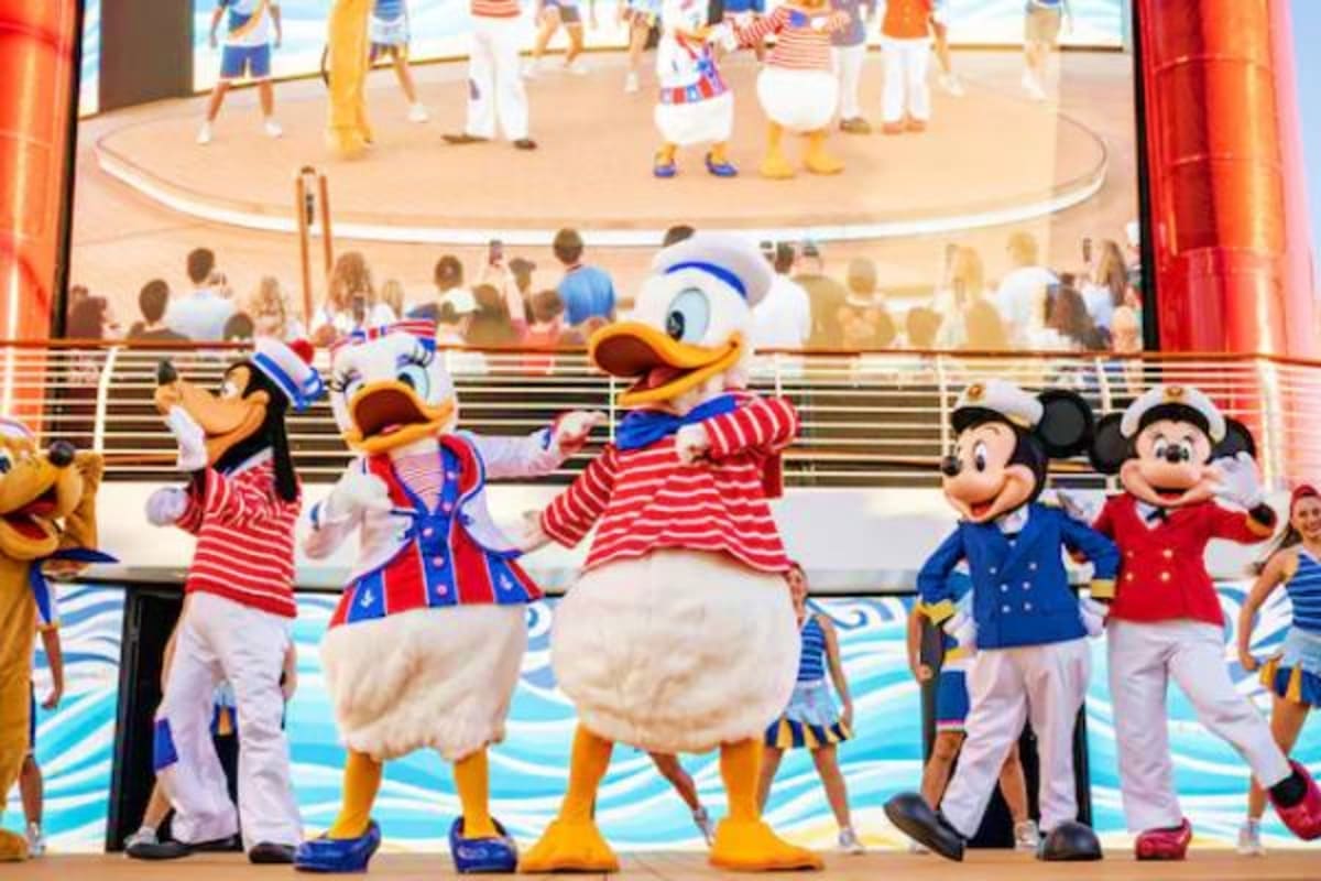 Disney characters in patriotic red and white striped outfits performing on a cruise ship deck with audience members watching 
