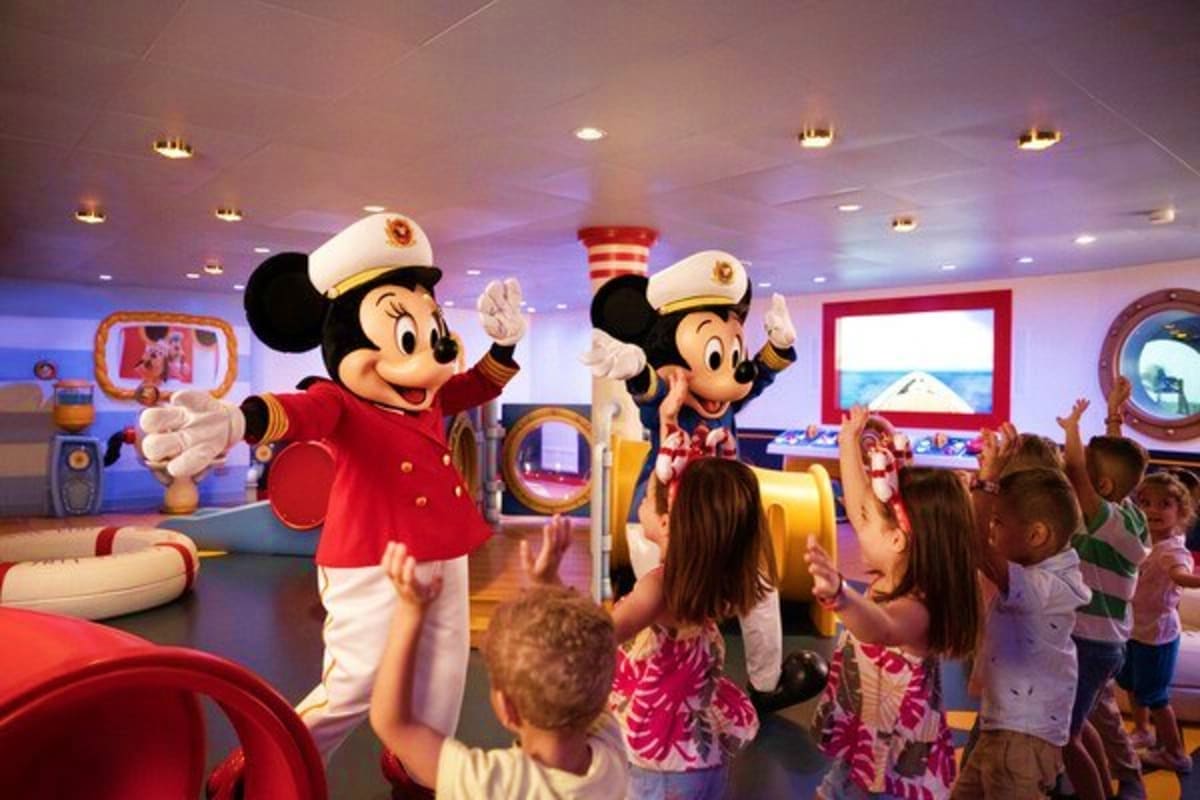 Mickey and Minnie Mouse in captain outfits greeting children in a colorful nautical-themed room on a Disney cruise ship