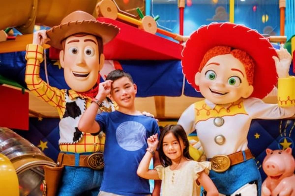 Children posing with Woody and Jessie characters at a toy-themed attraction in an indoor entertainment venue