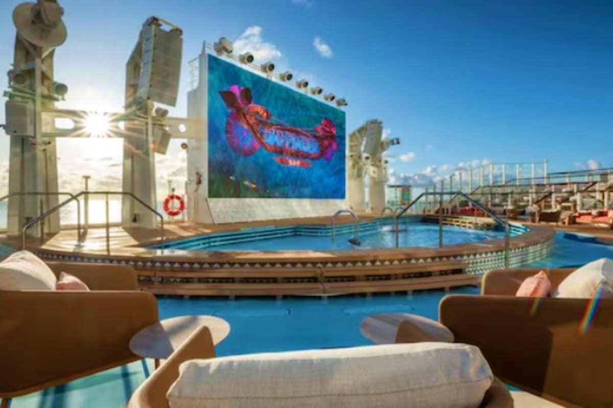 Cruise ship pool deck with lounge chairs, large digital screen displaying Disney logo, and ocean view under clear blue sky