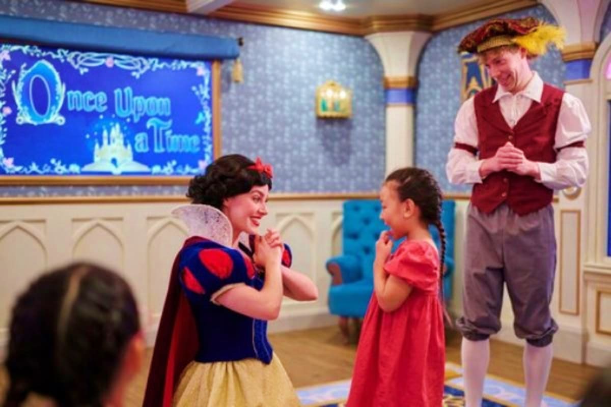 Disney character Snow White interacting with a young child in red dress during a themed cruise ship entertainment experience
