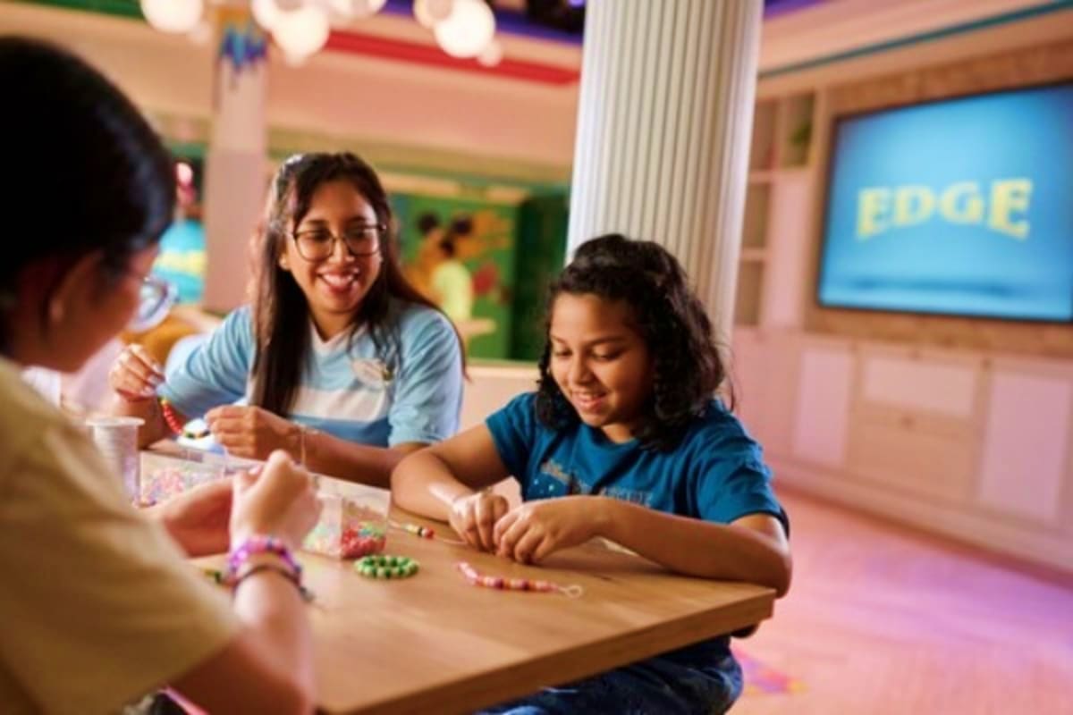 Students in a classroom engaging in a beaded bracelet craft activity at a table with colorful beads and string