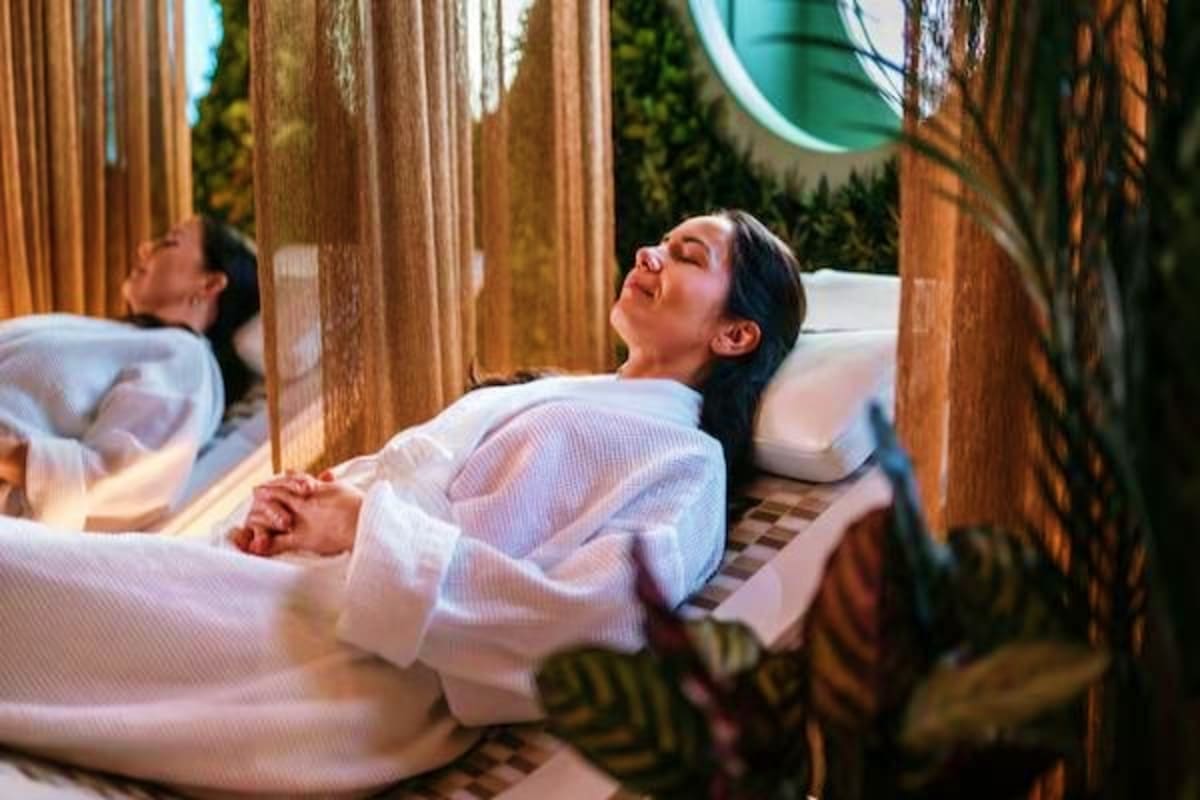 Woman relaxing in outdoor spa bath surrounded by wooden pillars and lush greenery at a tropical resort