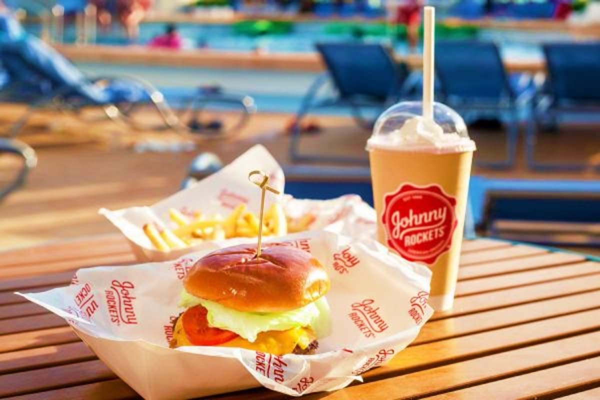 Johnny Rockets burger meal with fries and drink on poolside table with beach chairs and swimming pool in background
