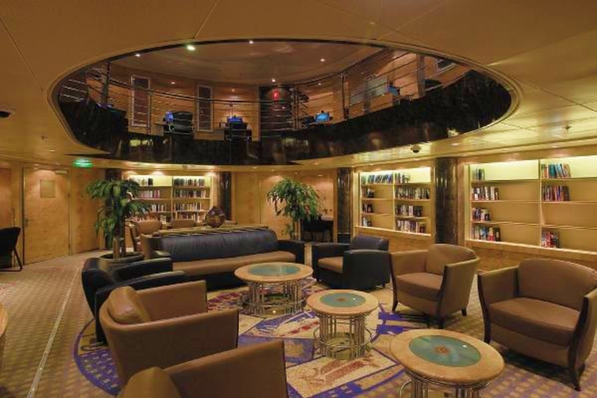 Modern library lounge with curved wooden bookshelves, beige armchairs, side tables, and circular skylight opening above