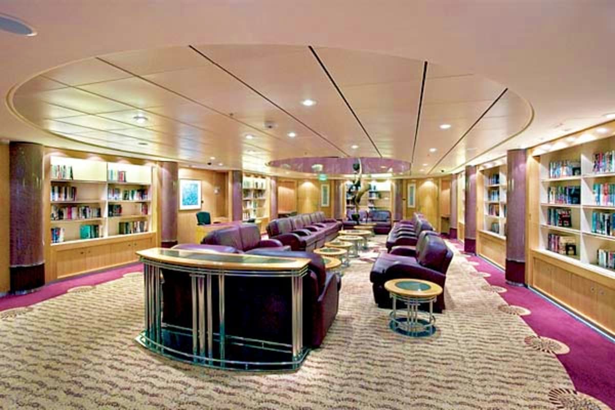 Modern cruise ship library with wooden bookshelves, purple seating areas, curved bar counter, and recessed ceiling lights
