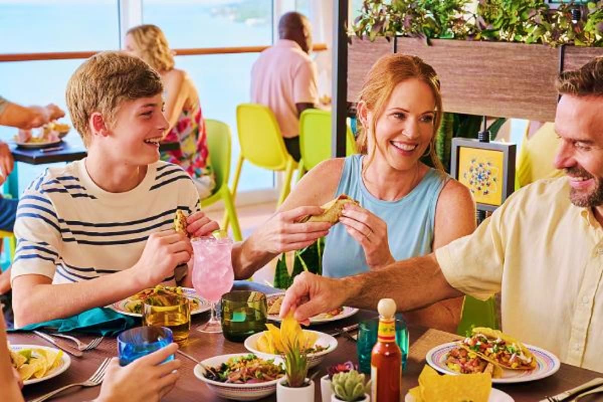 Family dining together at restaurant with ocean view, enjoying burgers and drinks on bright sunny day