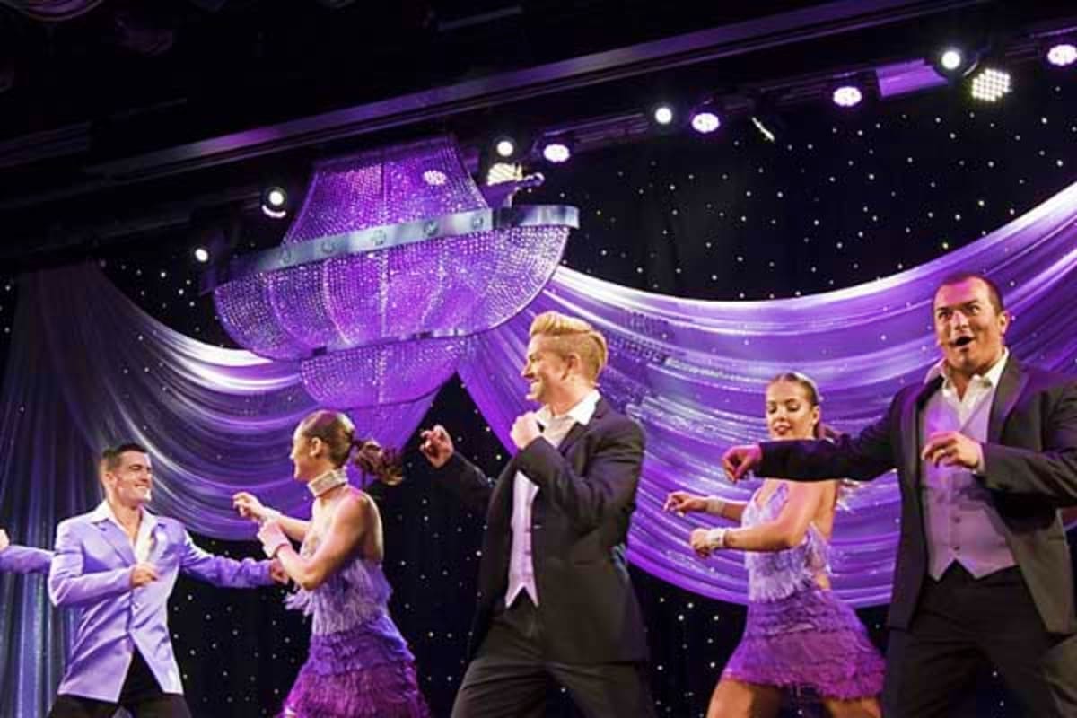 Group of performers on stage with purple lighting and sparkly spaceship prop in background