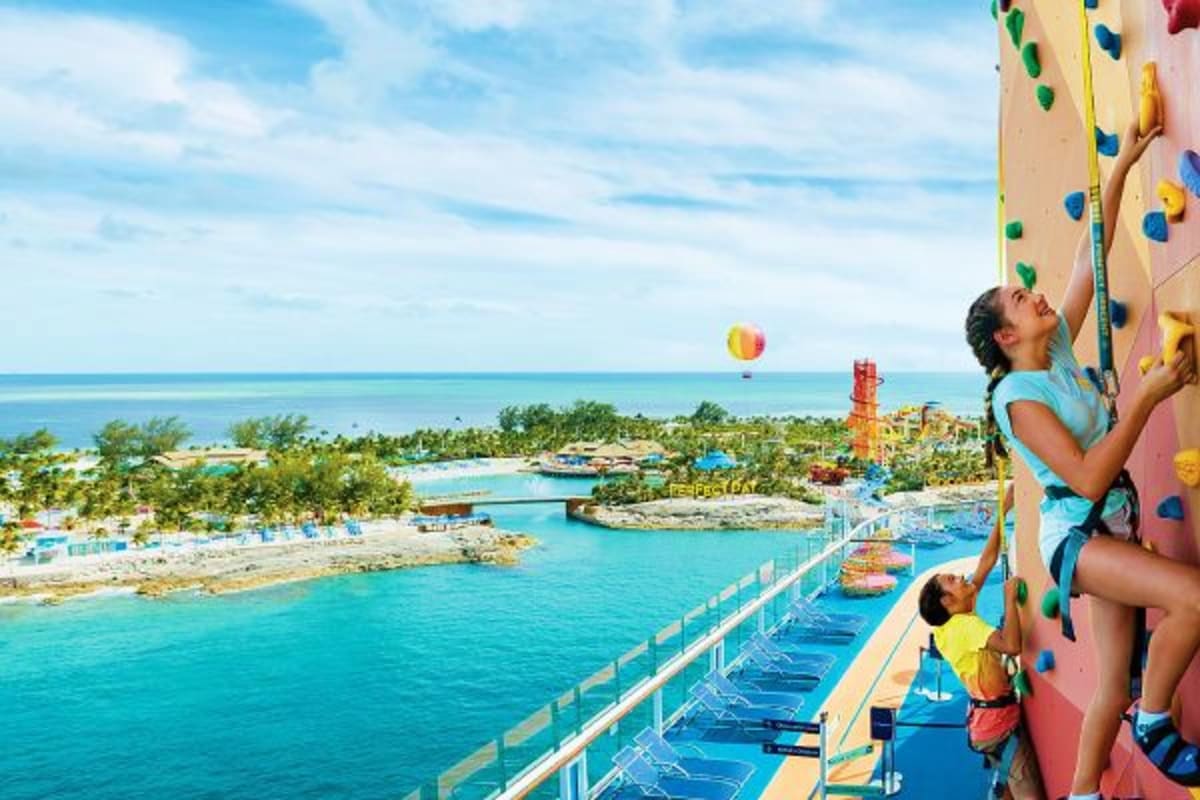 Woman and child rock climbing on cruise ship with tropical beach and ocean views below