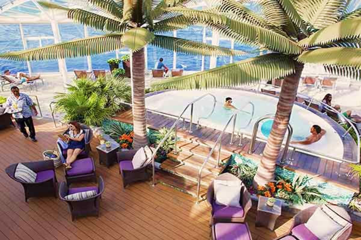 Cruise ship deck with hot tubs, lounge seating, palm trees, and ocean view in background