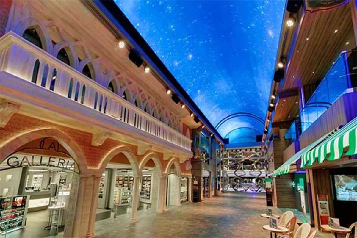 Indoor shopping promenade with starry blue ceiling, classical architecture, and retail storefronts on cruise ship