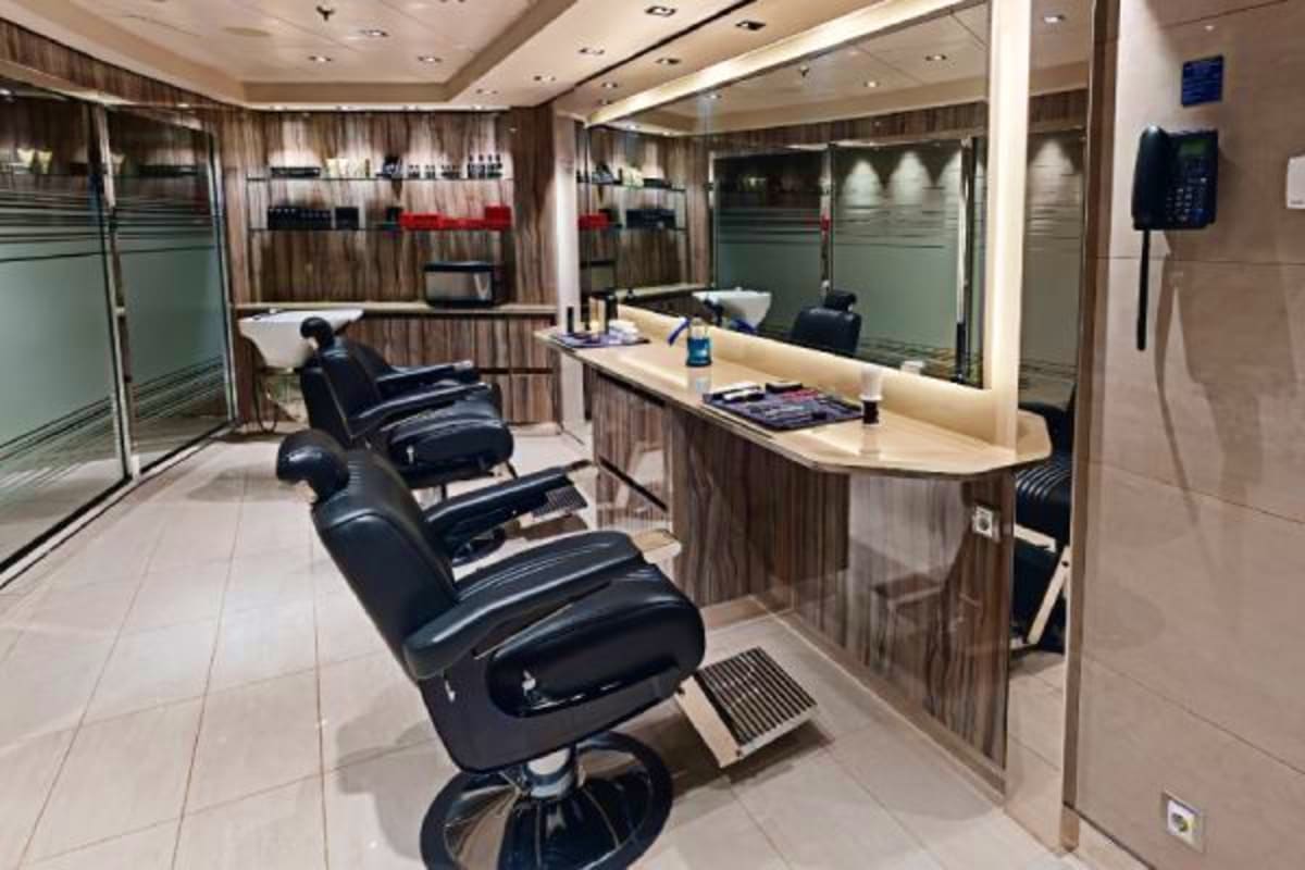 Modern barber shop interior on cruise ship with black hydraulic chairs, mirrored stations, and curved reception desk