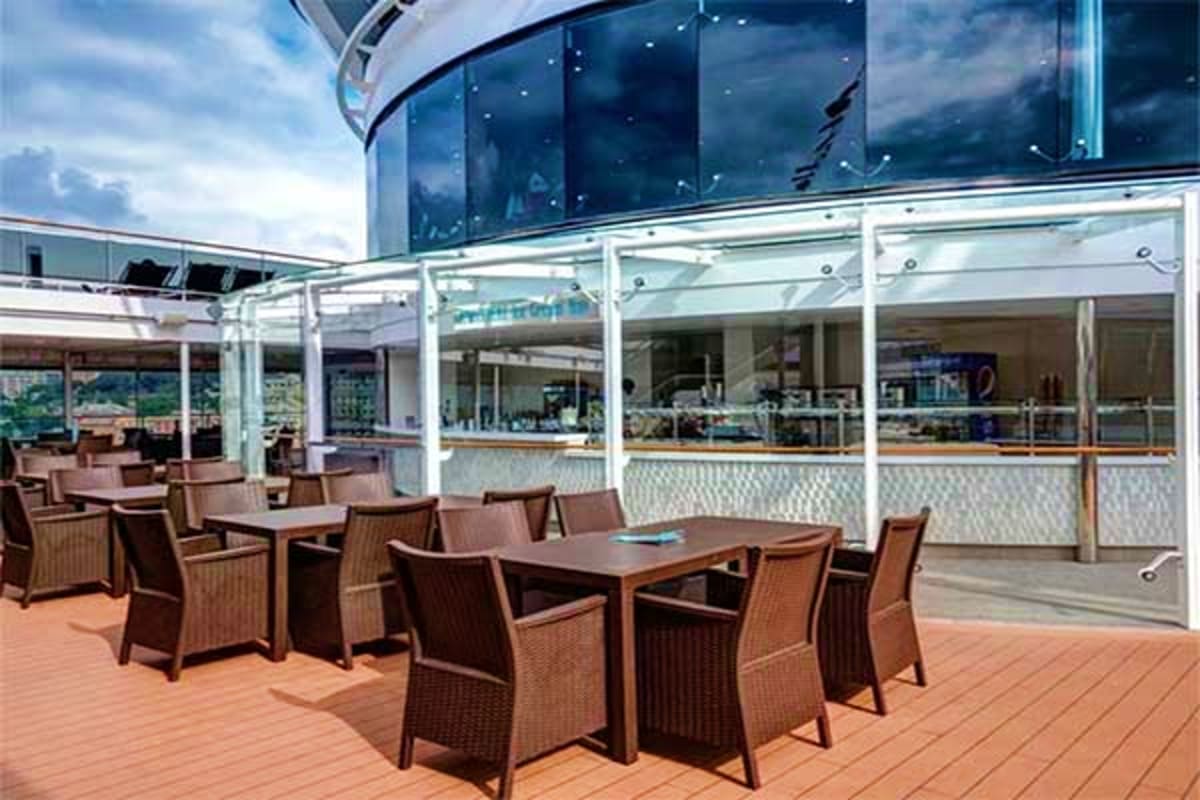 Outdoor deck area on MSC Euribia cruise ship with wicker chairs, dining tables, and panoramic windows overlooking cloudy sky