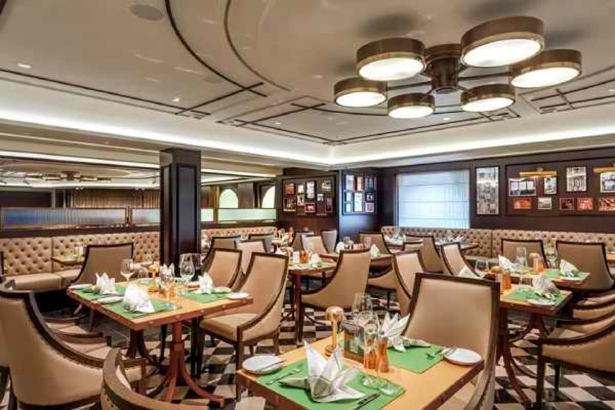 Elegant dining room aboard MSC Euribia with beige upholstered chairs, wood tables set with green linens, and modern ceiling f