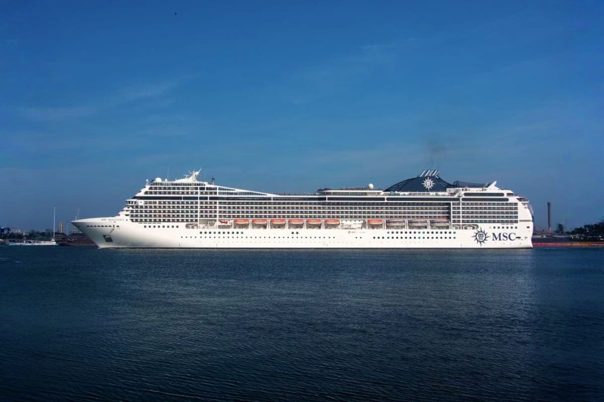 Large white MSC cruise ship on calm blue water with clear sky and port facilities visible in background