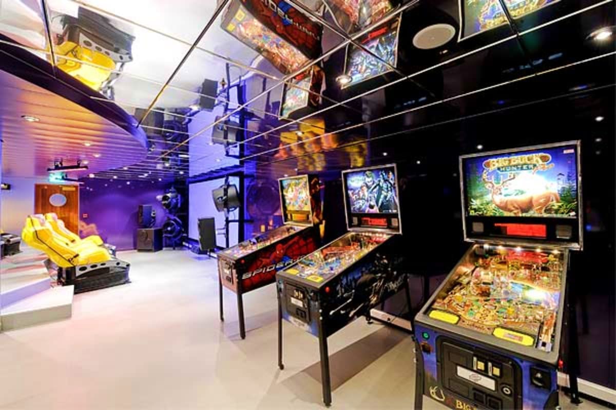 Modern arcade and entertainment room with pinball machines, vintage arcade cabinets, yellow racing simulator, and blue-purple