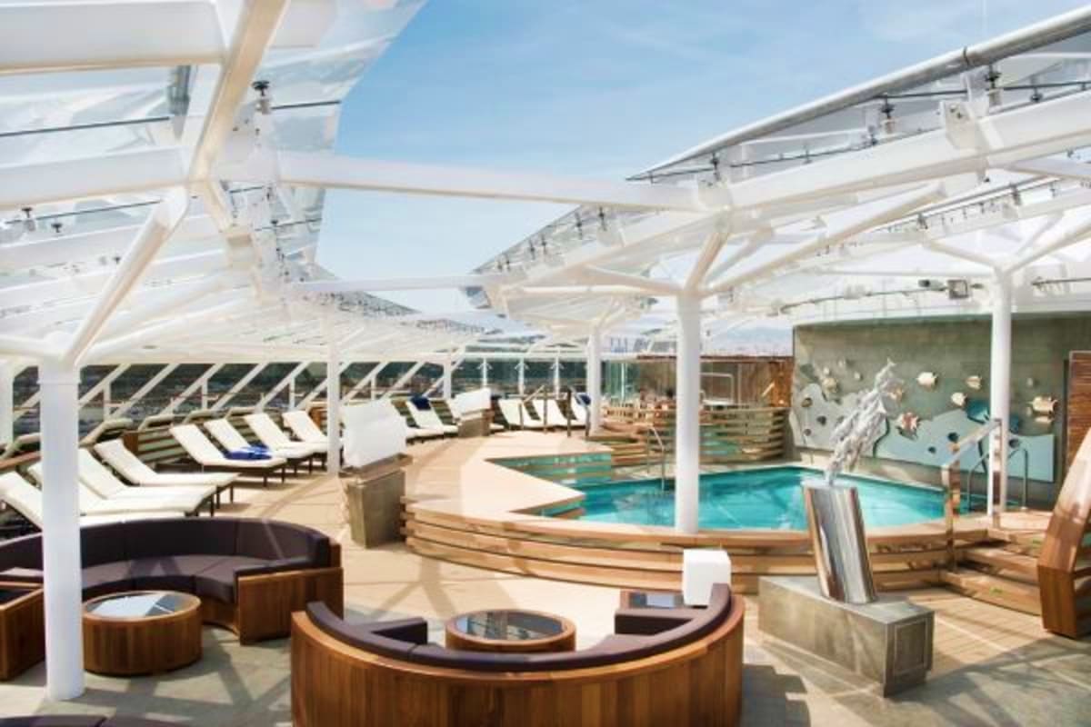 Luxury cruise ship pool deck with white retractable canopy, lounge chairs, swimming pools, and ocean view seating areas