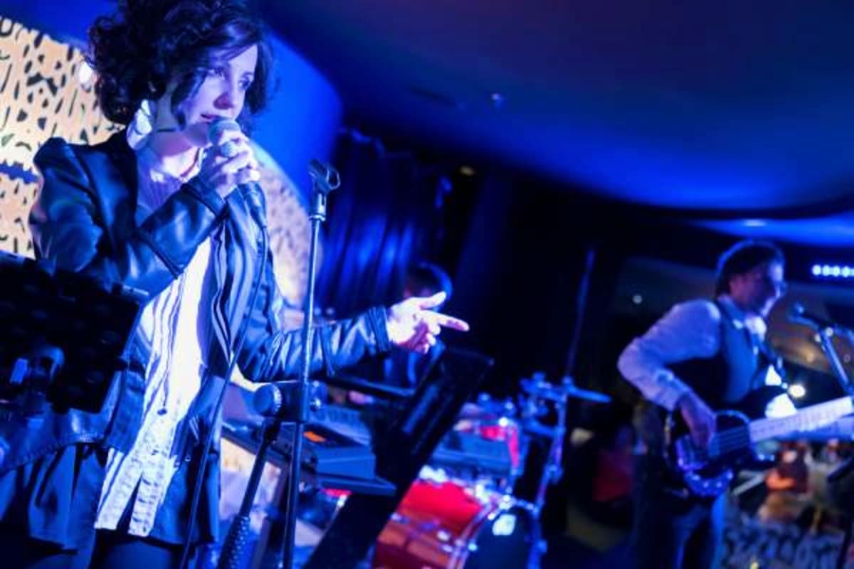 Live musical performance on stage with singer at microphone and band members under blue stage lighting during cruise entertai