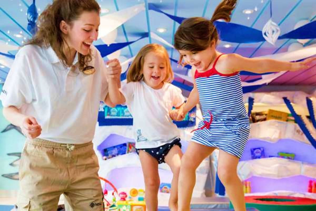 Three children playing and dancing together in a colorful indoor activity room on a cruise ship with blue decorative elements
