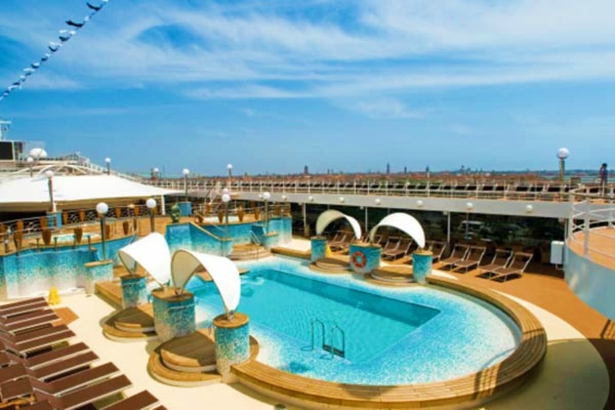 MSC Magnifica cruise ship pool deck with multiple swimming pools, sun loungers, white shade canopies, and ocean view under bl