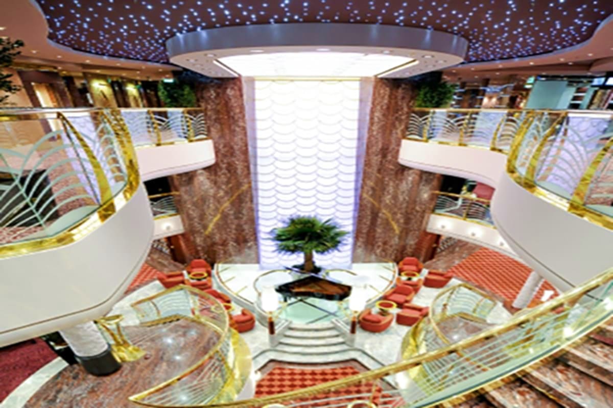 Luxurious multi-deck cruise ship atrium with starlit ceiling, curved balconies, gold railings, potted tree, and red seating a