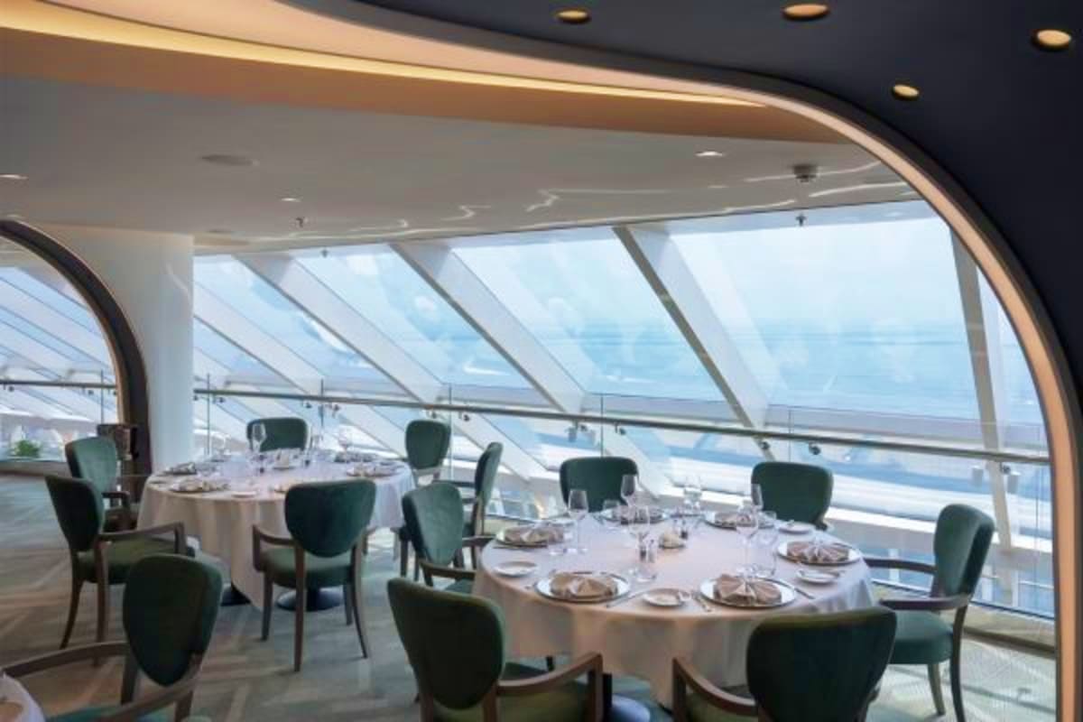 Elegant dining room on MSC Magnifica with round tables, green chairs, and panoramic ocean views through floor-to-ceiling wind