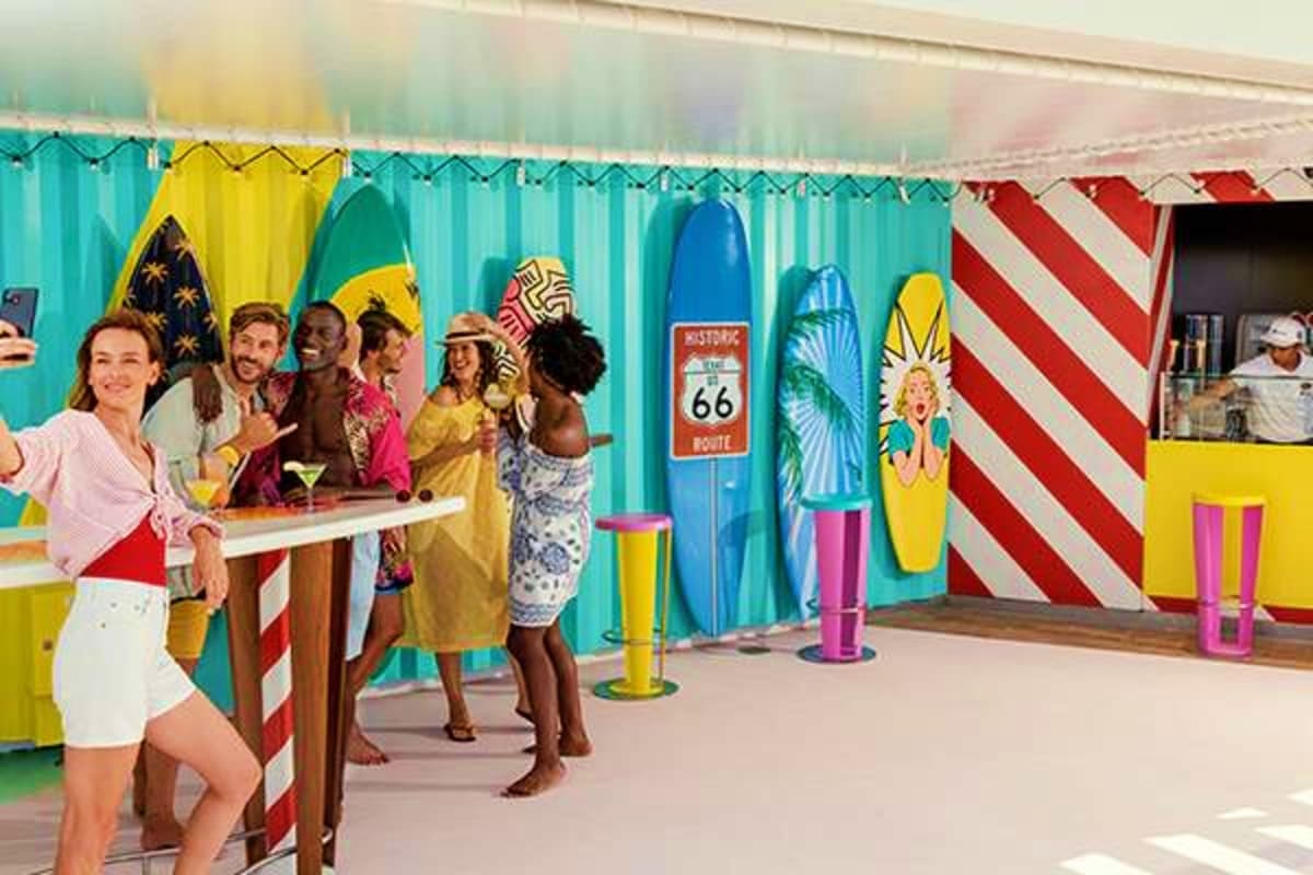 Diverse group of passengers enjoying beachside bar at cruise ship terminal with colorful surfboard decorations and Route 66 s