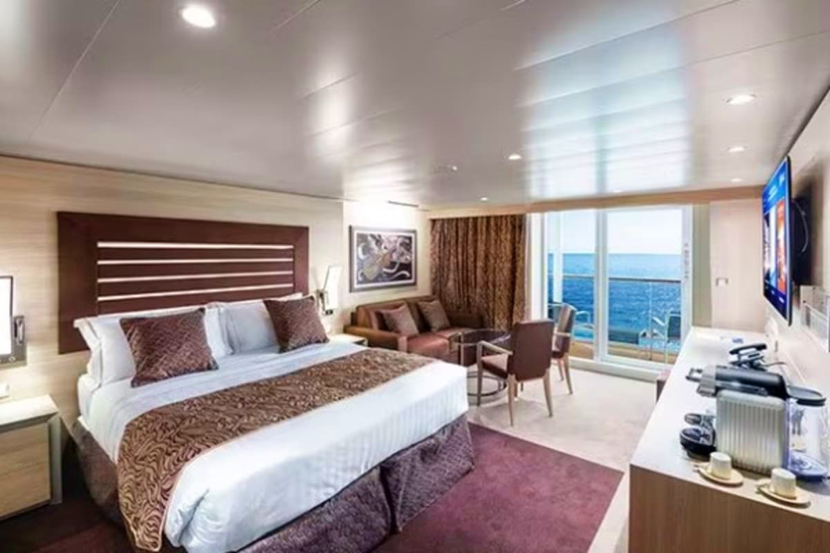 Luxurious cruise ship cabin with ocean view balcony, king bed, seating area, and modern amenities overlooking blue sea