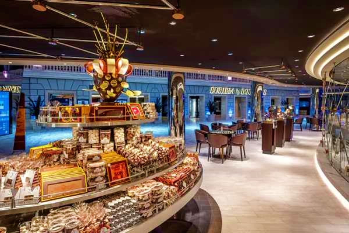 Luxurious cruise ship interior atrium with tiered gold and red decorative display, modern curved ceiling with recessed lighti