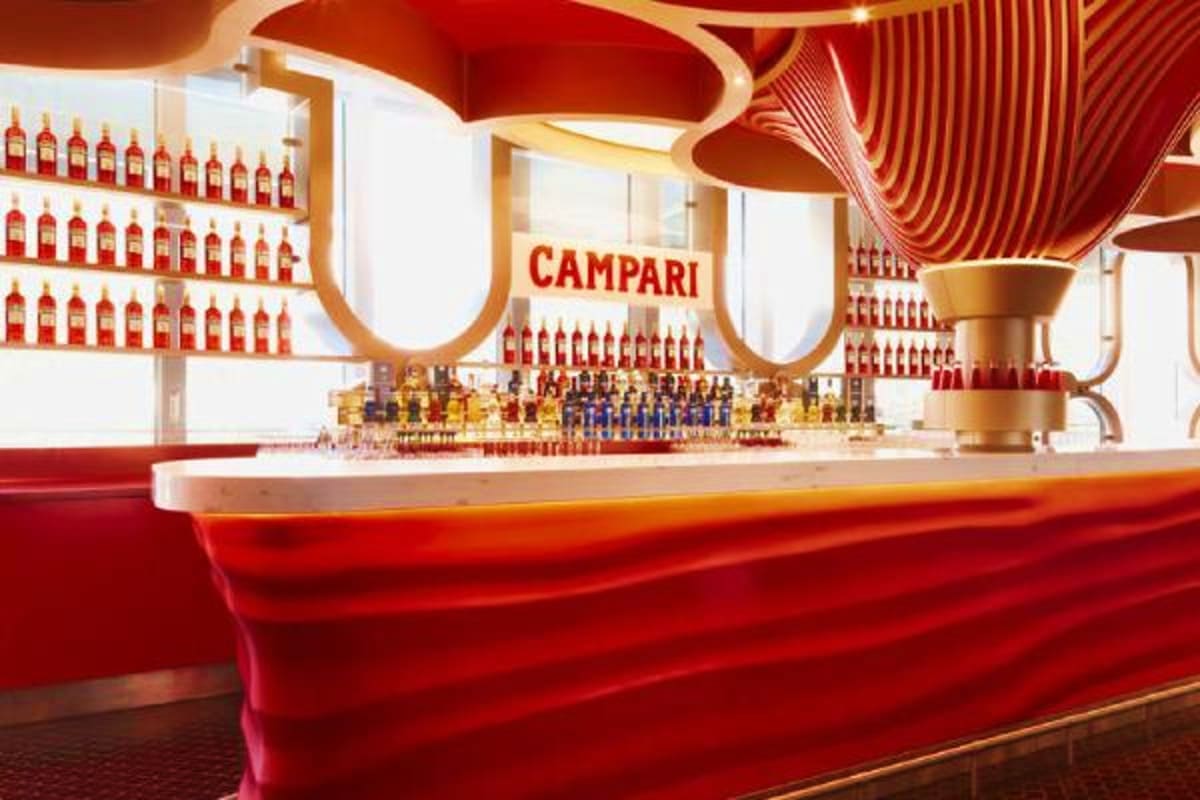 Modern Campari bar interior with red and gold curved ceiling design, illuminated bottles displayed on white walls, and sleek 
