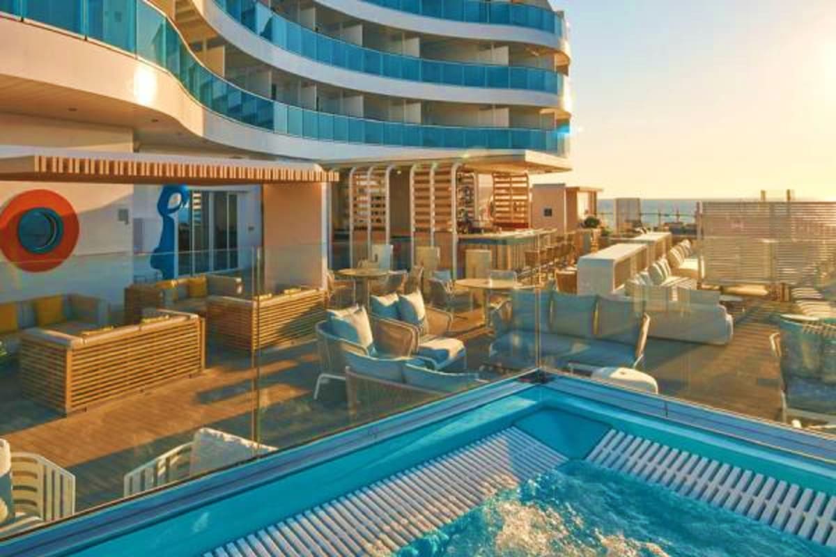 Luxury cruise ship deck with swimming pool, wooden lounge chairs, and curved modern building with blue-tinted balconies at su